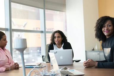 Formatrice présentant un support de travail à une professionnelle dans un bureau lumineux.